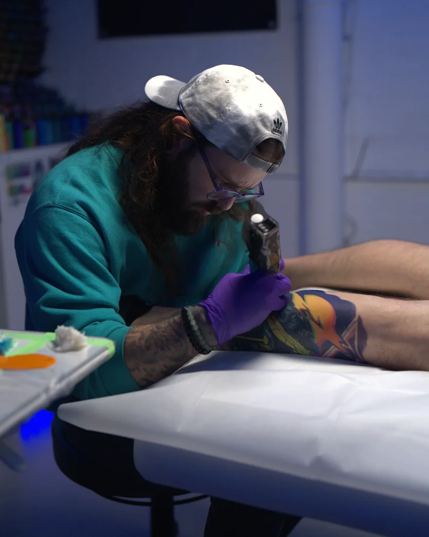 Bobby Cupparo in a teal sweater tattooing a client in his Austin, Texas studio