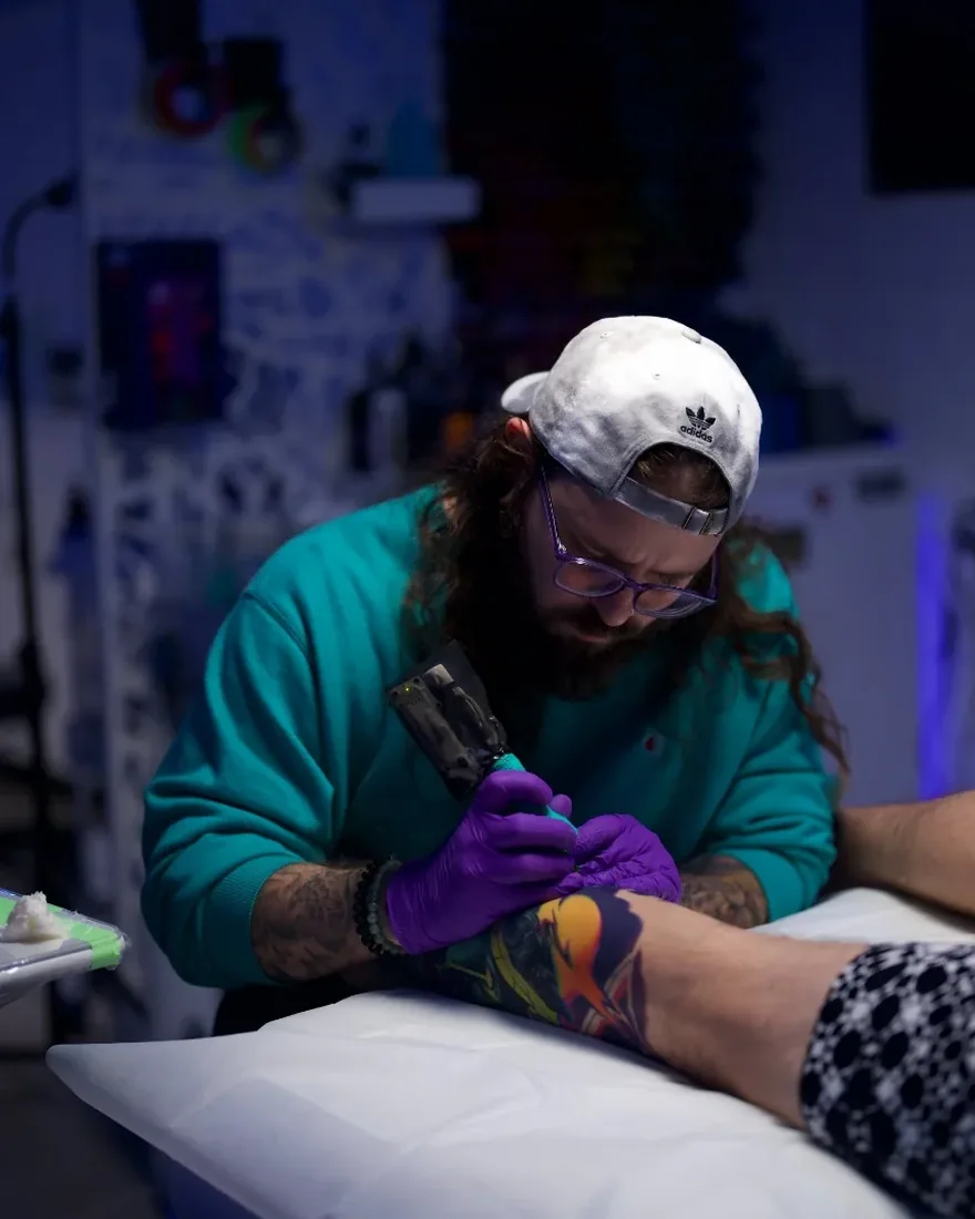 Bobby Cupparo in a teal sweater tattooing a client in his Austin, Texas studio