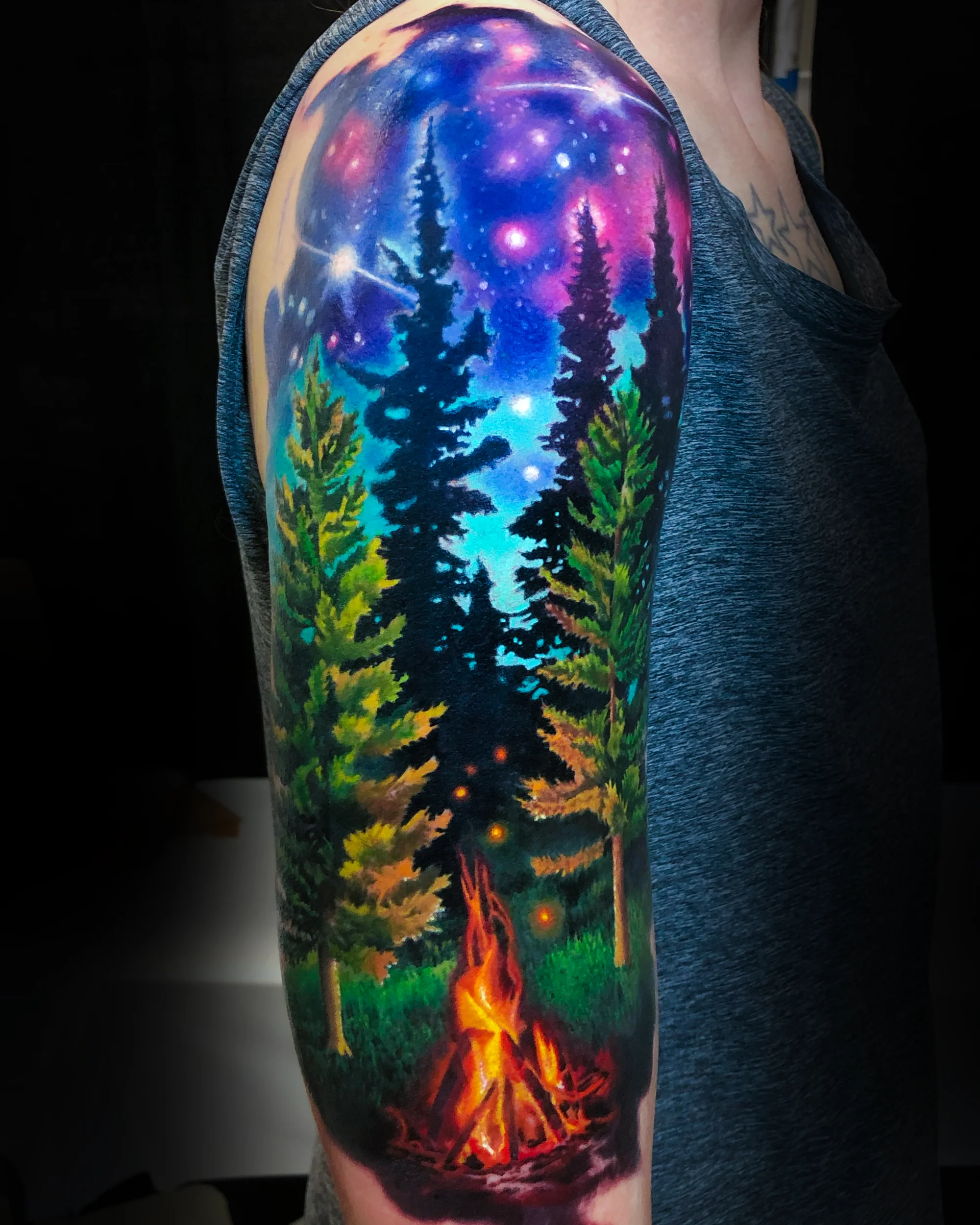 Color realism forest campfire galaxy upper arm tattoo by Austin tattoo artist Bobby Cupparo