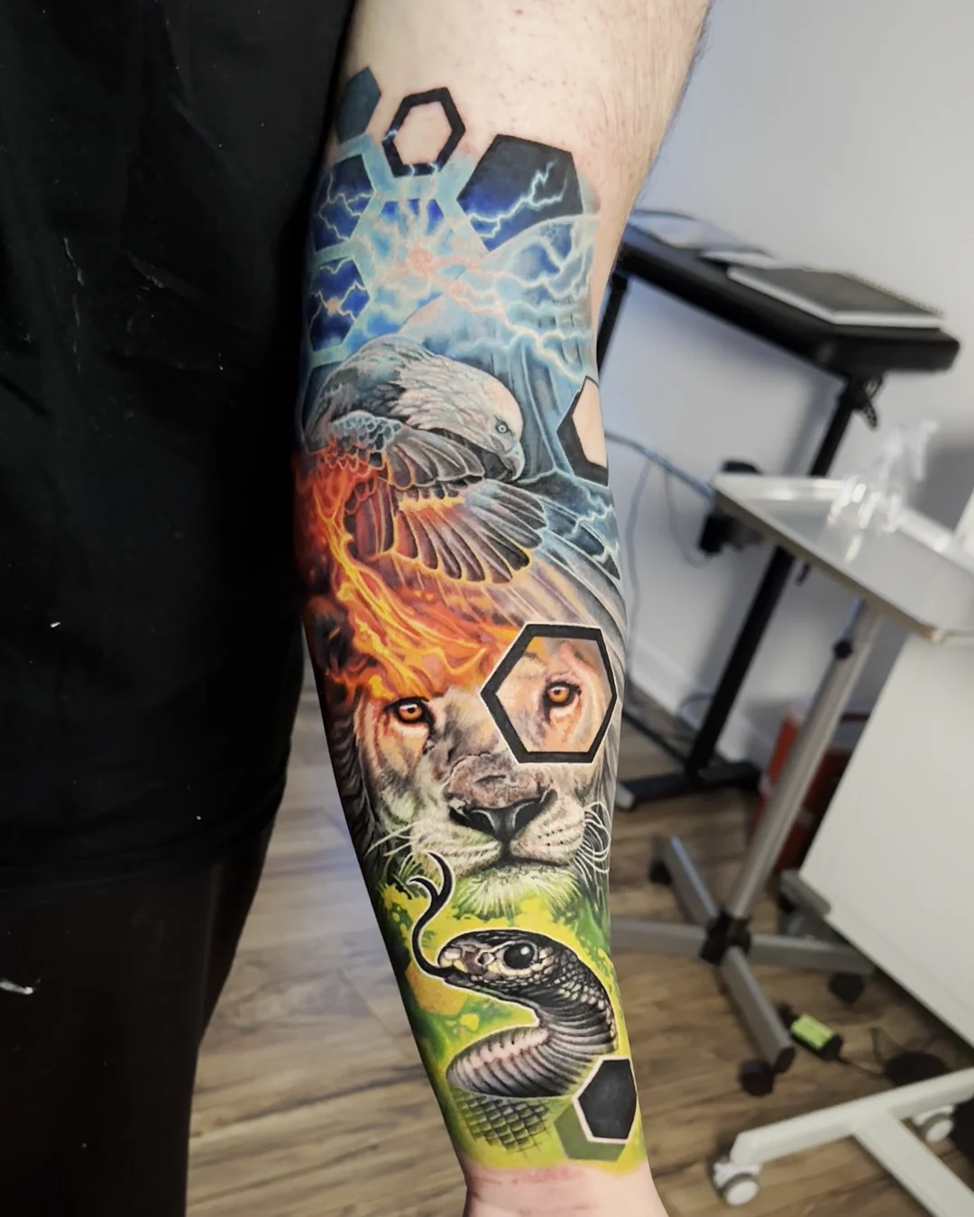 Color realism lion with a fire mane, eagle and black snake with hexagons and lightning, forearm tattoo by Austin tattoo artist Bobby Cupparo