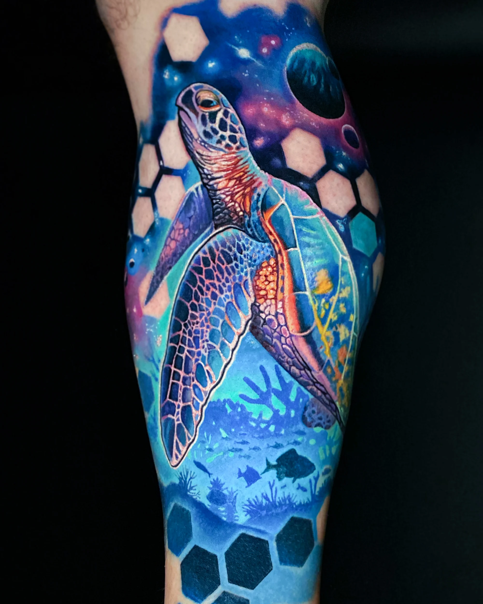Color realism sea turtle swimming up from a coral reef into a galaxy with planets and hexagons, calf tattoo by Austin tattoo artist Bobby Cupparo