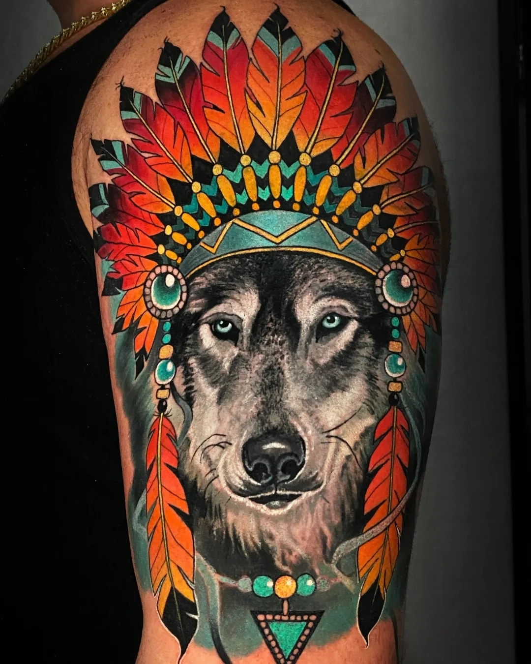 Color realism wolf portrait with vibrant feather headdress upper arm tattoo by Austin tattoo artist Bobby Cupparo