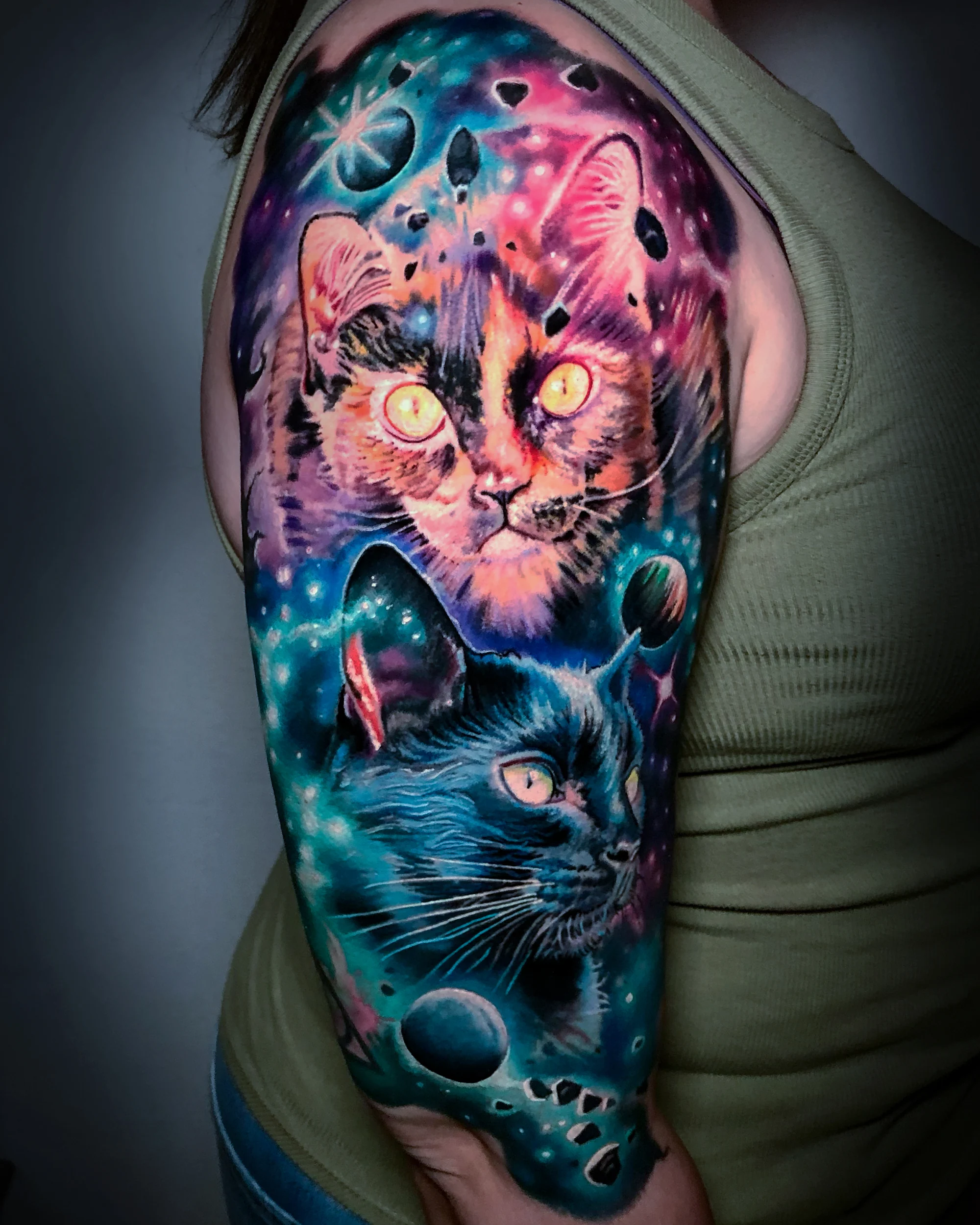 Color realism portrait of two cats in a galaxy, a glowing orange and pink cat above a blue-black cat, with planets and stars, upper arm tattoo by Austin tattoo artist Bobby Cupparo