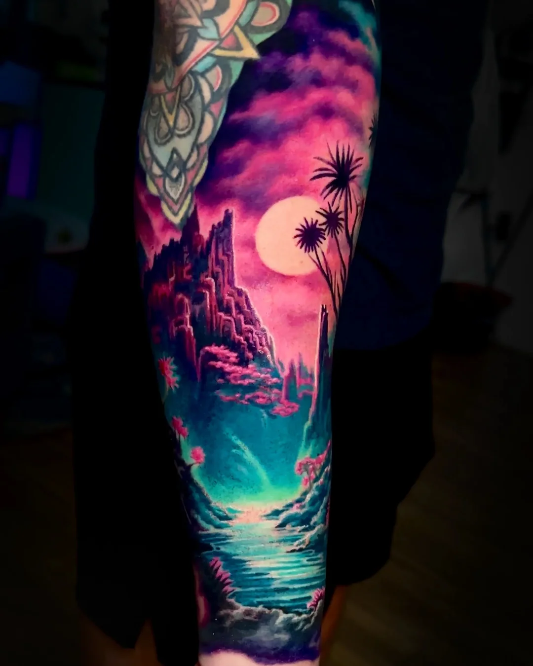 Surreal color fantasy moonlit cliff ruins with teal lagoon and pink sky forearm tattoo by Austin tattoo artist Bobby Cupparo