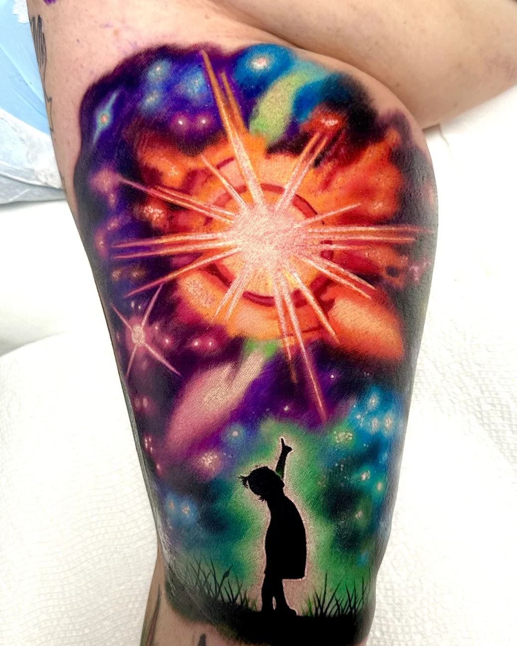 Surreal color galaxy starburst with a child silhouette reaching up, thigh tattoo by Austin tattoo artist Bobby Cupparo