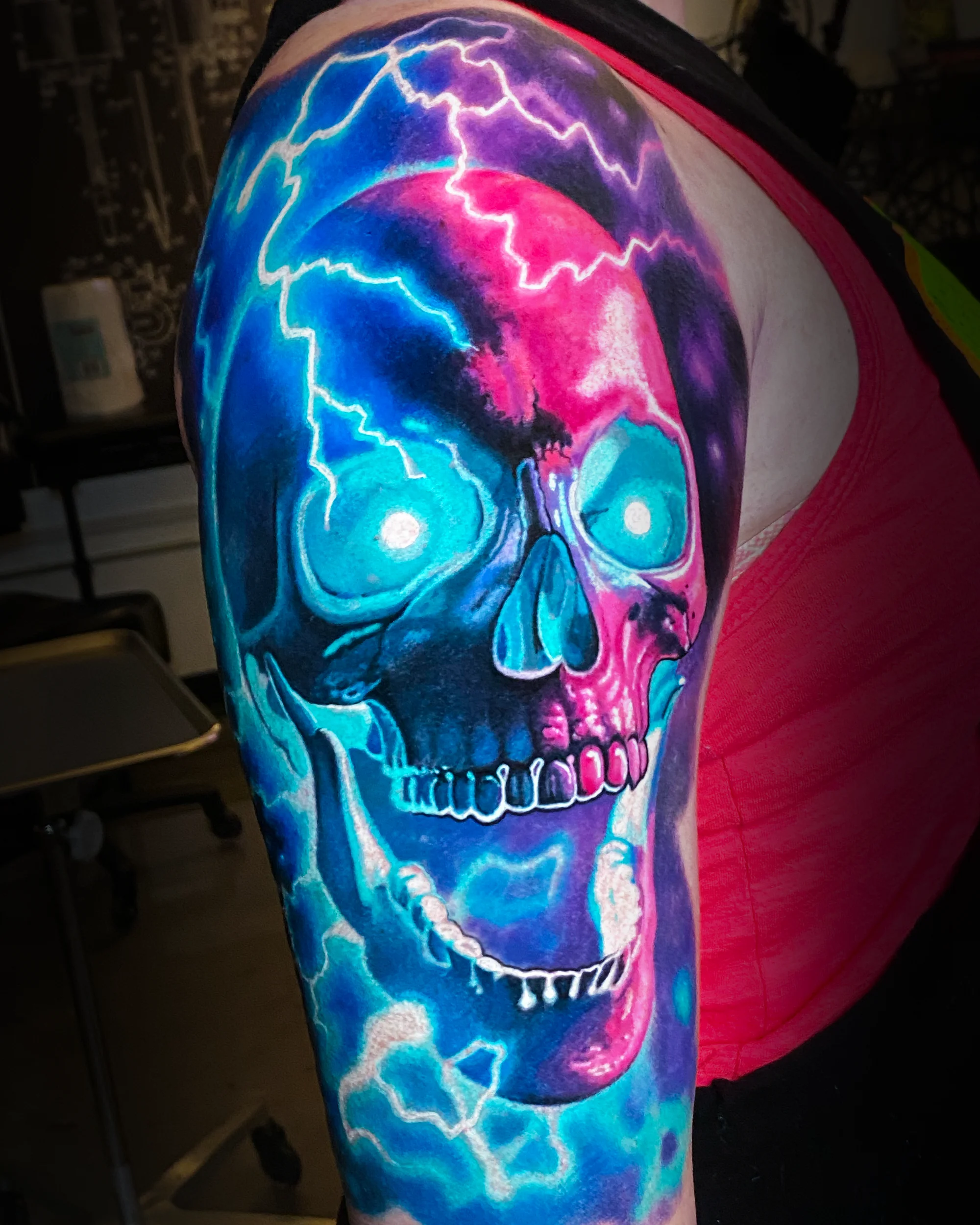 Surreal color electric lightning skull blue pink upper arm tattoo by Austin tattoo artist Bobby Cupparo