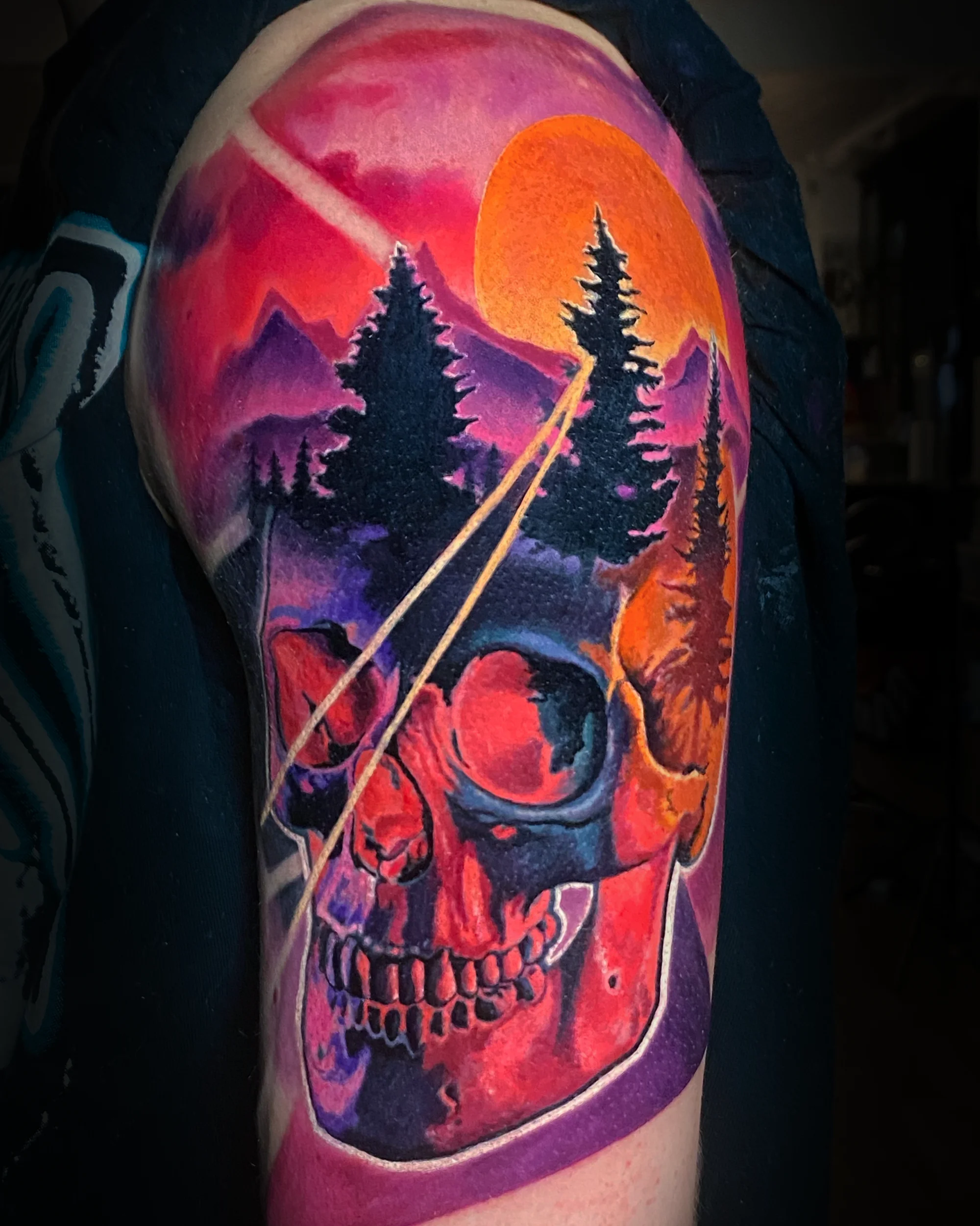 Surreal color skull with mountain sunset forest upper arm tattoo by Austin tattoo artist Bobby Cupparo
