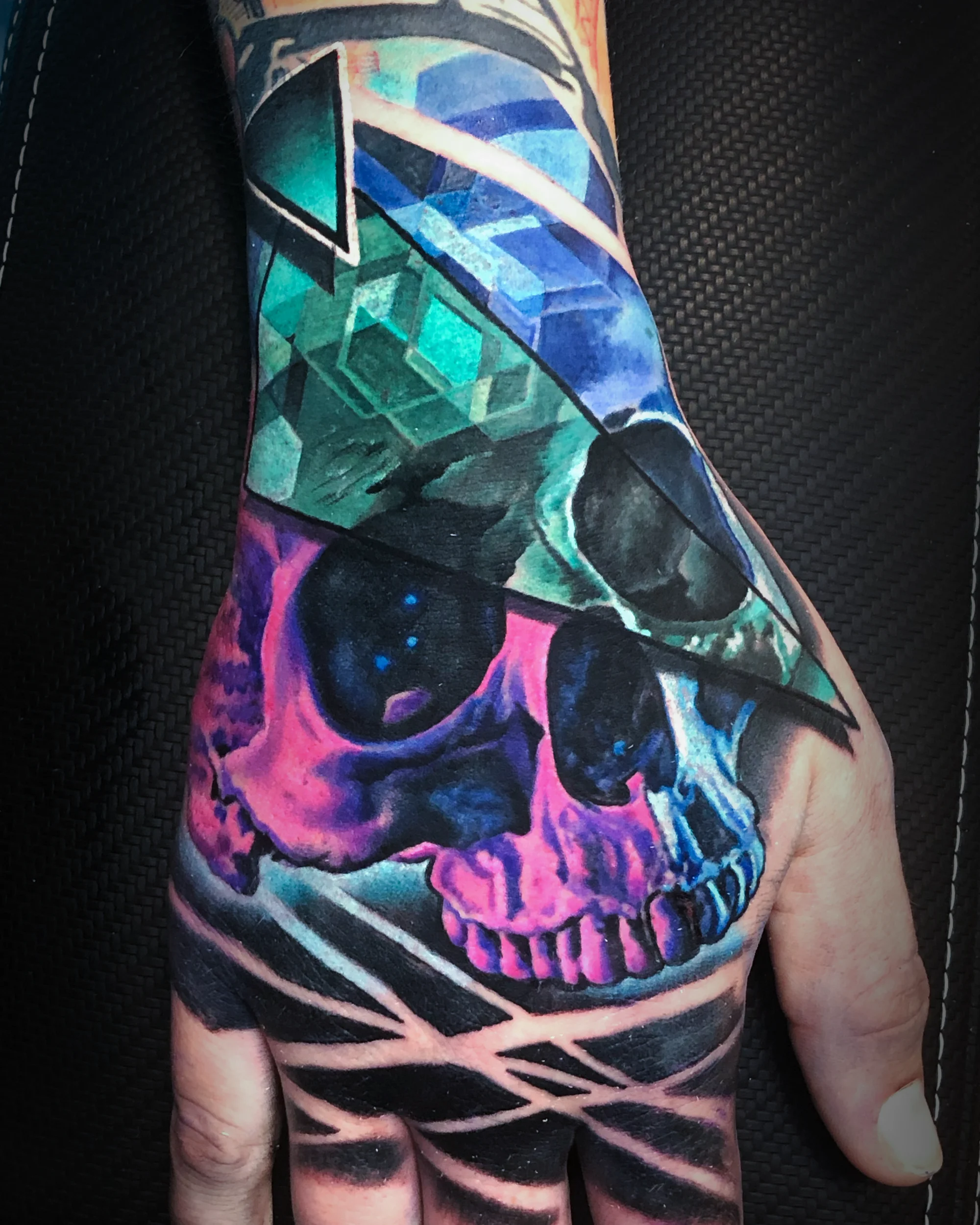Surreal color geometric skull pink teal hand tattoo by Austin tattoo artist Bobby Cupparo