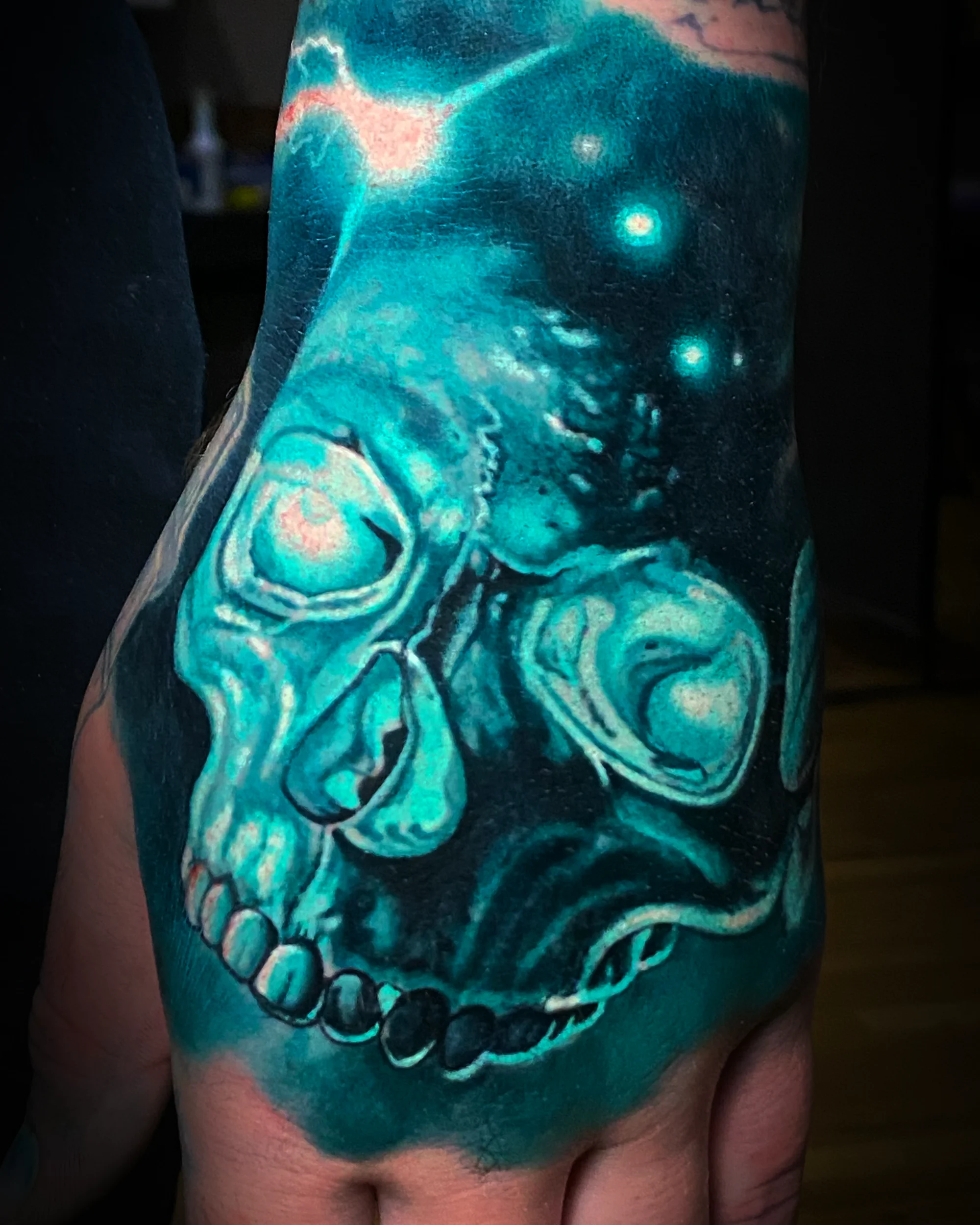 Surreal color teal monochromatic skull galaxy hand tattoo by Austin tattoo artist Bobby Cupparo